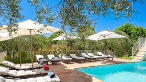 Area piscina con lettini e ombrelloni, una piscina blu cristallina e una scalinata che conduce a un livello superiore.