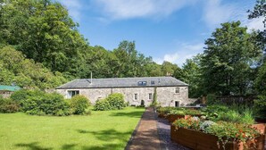A stone building with a paved pathway leading to the entrance, surrounded by lush greenery and a well-maintained garden.