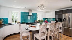 A modern kitchen with a central island, white cabinetry, and a teal backsplash.