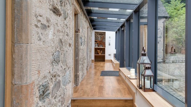 A narrow hallway with a wooden floor, a stone wall, and a glass ceiling.