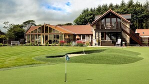 Golfkenttä, jonka yhteydessä on kerhotila, jossa on suuri lasijulkisivu, kiviverhous ja puinen terassi.