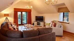 A spacious living room with a large TV, a sofa, a coffee table, and a chandelier. - St Andrews Round House (Cupar)