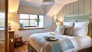 A bedroom with a large bed, a window with a view, a bedside table with a lamp, and a suitcase on the floor. - St Andrews Round House (Cupar)