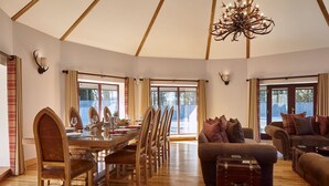 A spacious room with a dining table set for four, wooden chairs, a leather sofa, and a large window with curtains. - St Andrews Round House (Cupar)