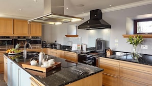 A modern kitchen with stainless steel appliances, wooden cabinets, and a black island with a coffee station. - St Andrews Round House (Cupar)