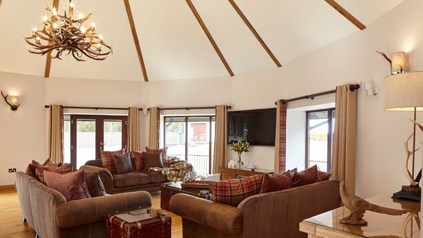 A spacious living room with two sofas, a wooden coffee table, a vintage suitcase, and a chandelier. - St Andrews Round House (Cupar)
