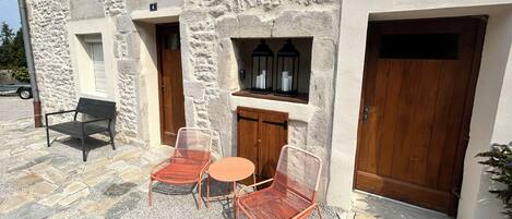 Un edificio de piedra con puerta de madera, ventana con un cartel de número y terraza con sillas y mesa de metal.
