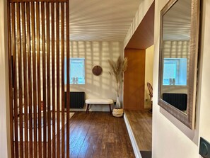 Un couloir avec une cloison en bois, un banc, un vase contenant des plantes séchées et un miroir accroché au mur.