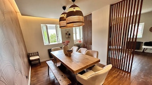 A dining area with a wooden table, benches, and chairs. There are two hanging light fixtures above the table. - Ferme Gabriela | Luxury accommodation in the lake region in the heart of the Jura mountains (Châtillon)