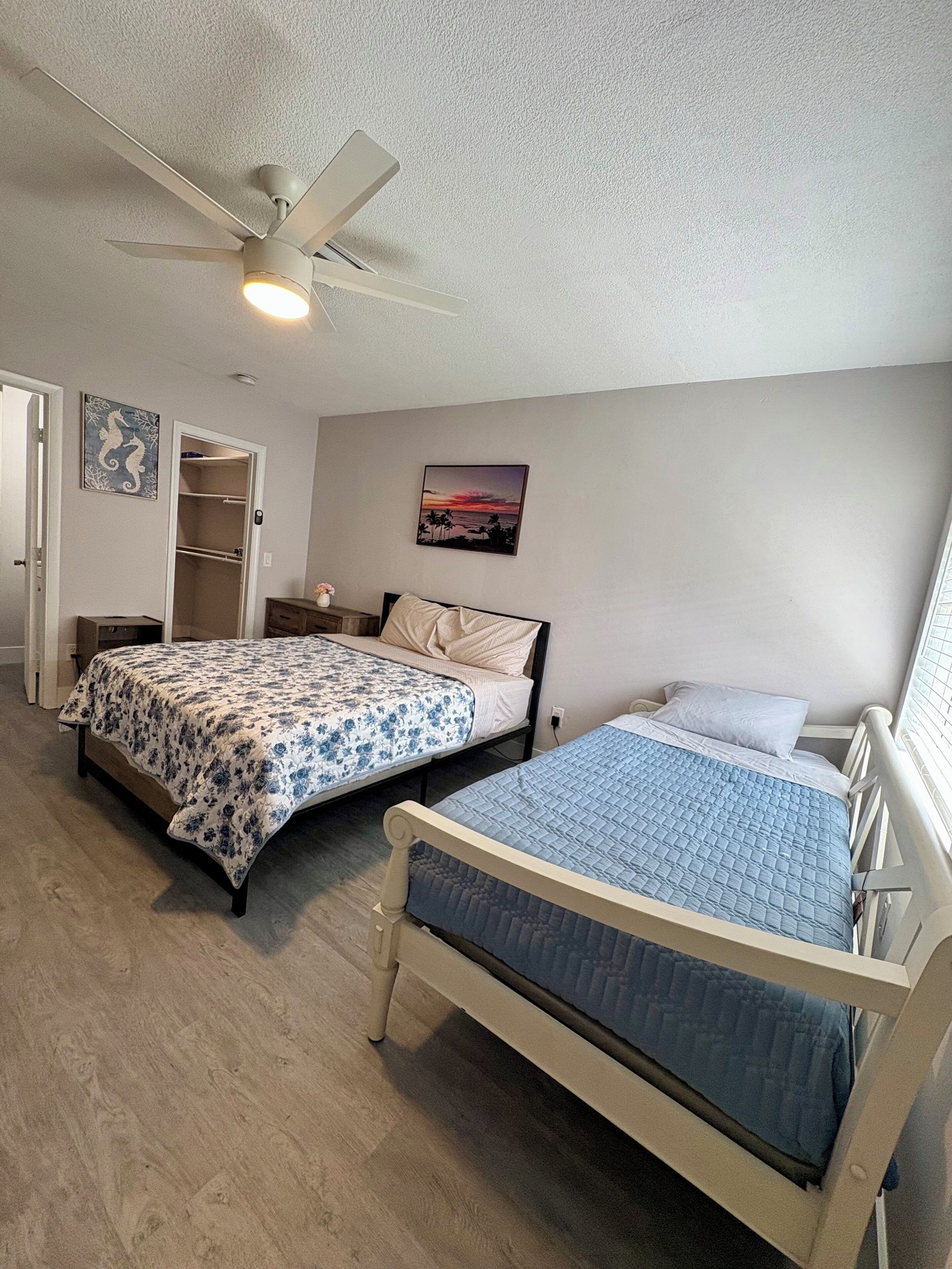 A bedroom with two beds, a ceiling fan, a closet, and a painting on the wall.