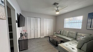 A living room with a sofa, coffee table, TV, and closet doors. - Cozy 1-bed apt in fabulous Pompano Beach across from the beach, AC, WiFi, pets (Pompano Beach)