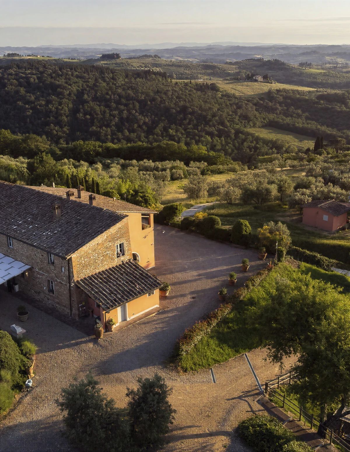 Una tenuta rurale con un grande edificio in pietra, un vialetto sterrato e vegetazione circostante.