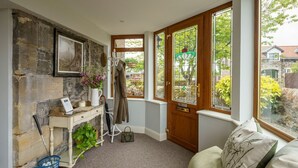 Une pièce chaleureuse avec un mur en pierre, une porte en bois ornée de vitraux, une petite table avec un ordinateur portable et une vue sur le jardin.