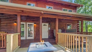 A log cabin with a covered deck, a fire pit, and a door with a window. - Hot Tub, Fire Pit, WiFi, EV Charger | Biggie cabin near Red River Gorge, KY! (Stanton)