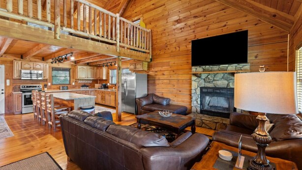 A spacious log cabin interior with a kitchen, dining area, and living room. - Hot Tub, Fire Pit, WiFi, EV Charger | Biggie cabin near Red River Gorge, KY! (Stanton)