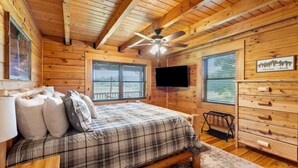 A cozy cabin bedroom with a plaid bedspread, a ceiling fan, and wooden walls. - Hot Tub, Fire Pit, WiFi, EV Charger | Biggie cabin near Red River Gorge, KY! (Stanton)