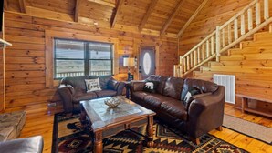 A cozy log cabin interior with a wooden staircase, leather sofas, and a central coffee table. - Hot Tub, Fire Pit, WiFi, EV Charger | Biggie cabin near Red River Gorge, KY! (Stanton)