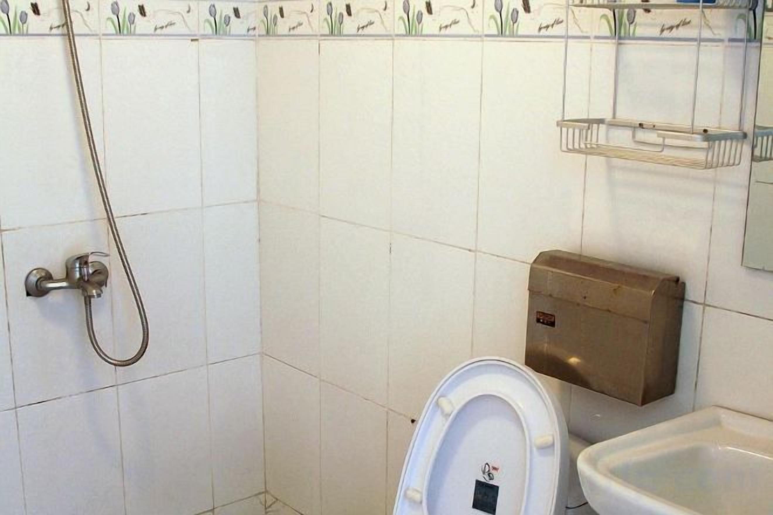 A bathroom with a toilet, a sink, a shower, and a soap dispenser.
