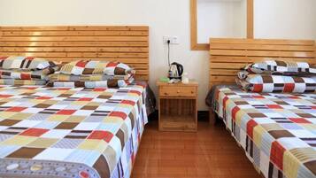 Una habitación con dos camas, cada una con cubrecama acolchado, cabecero de madera, mesita de noche con lámpara y espejo montado en la pared.