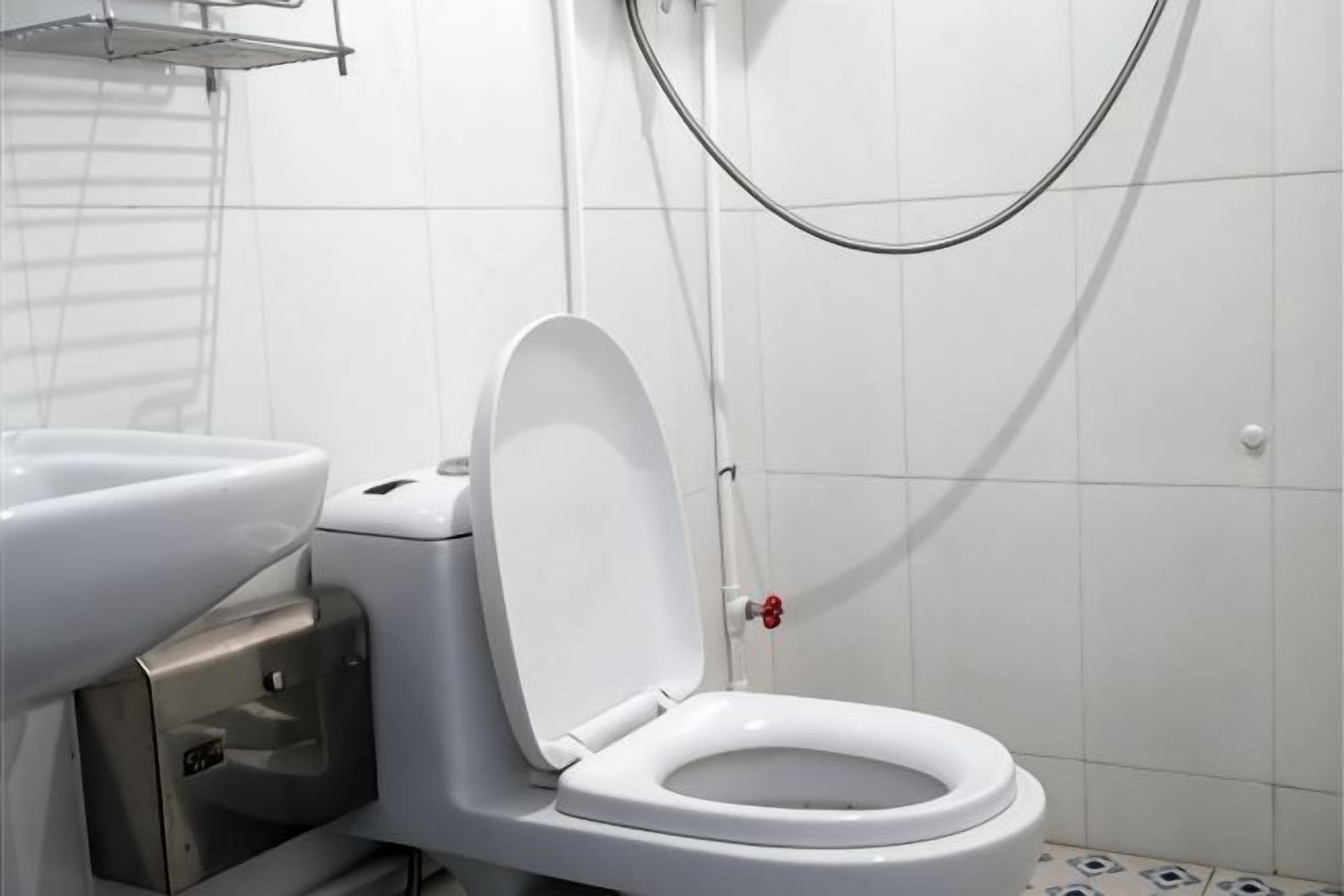 Un inodoro blanco con la tapa cerrada, un bidé y un cabezal de ducha en un baño con paredes de azulejos blancos.