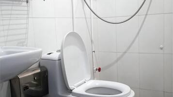 Un inodoro blanco con la tapa cerrada, un bidé y un cabezal de ducha en un baño con paredes de azulejos blancos.