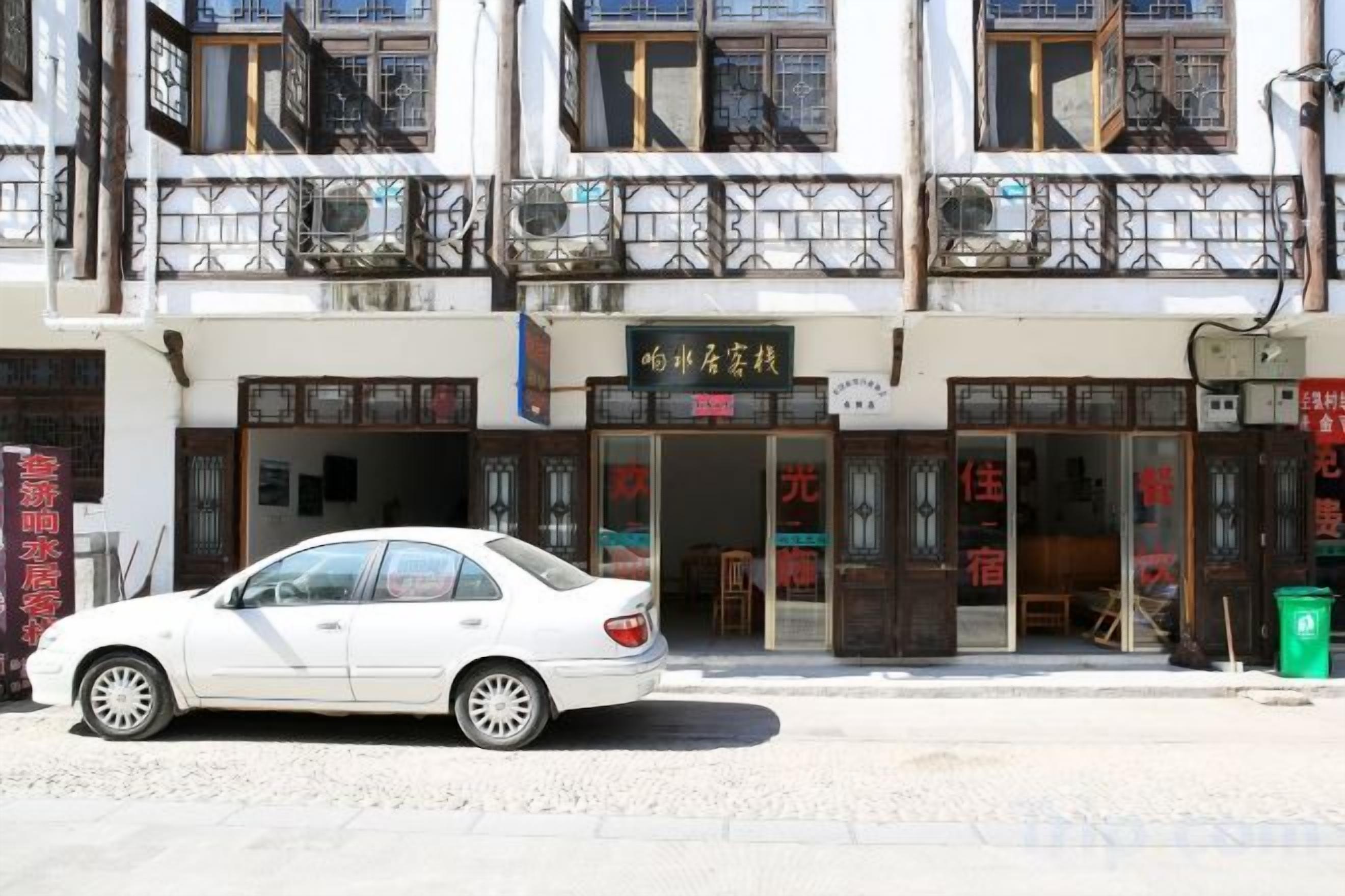 A white car parked in front of a building with a storefront.