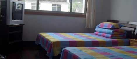 A room with two beds, a television, and a window with a view of buildings.