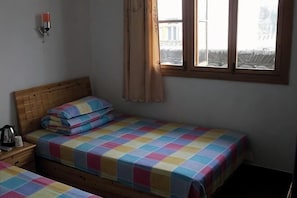 A room with two single beds, a wooden headboard, a bedside table with a lamp, and a window with curtains.