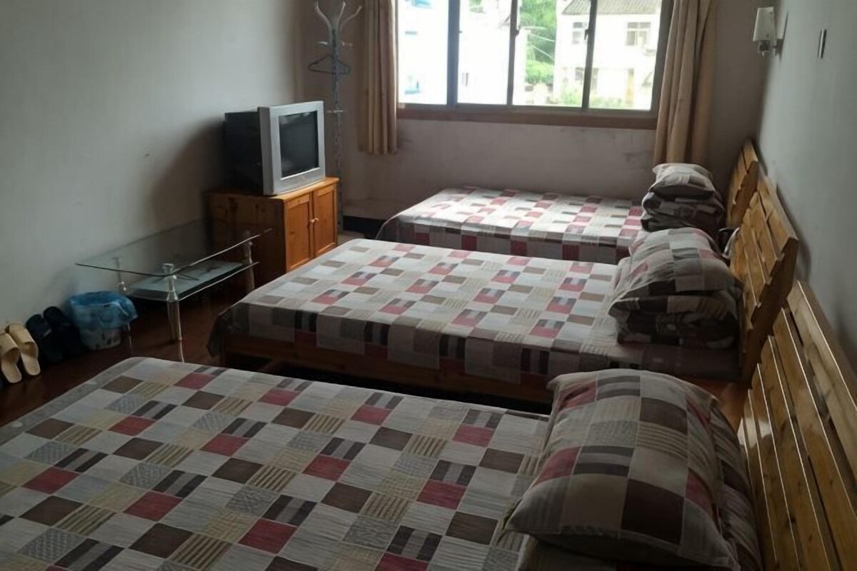 A room with two beds, a television, a wooden cabinet, and a window with curtains.