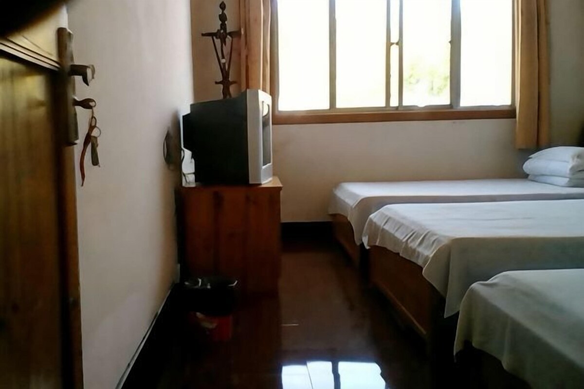 Une chambre avec deux lits, une commode en bois, une télévision et une fenêtre avec des rideaux.
