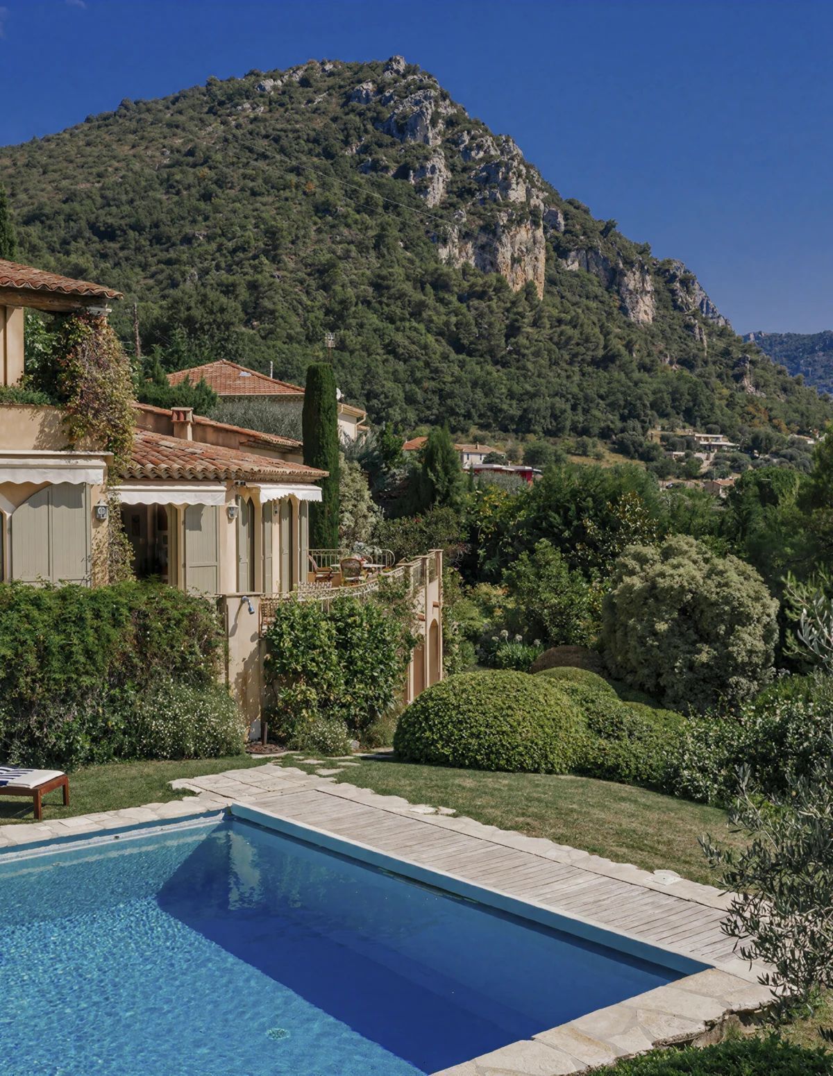 A swimming pool with a mountain backdrop, surrounded by lush greenery and a traditional building with a tiled roof.