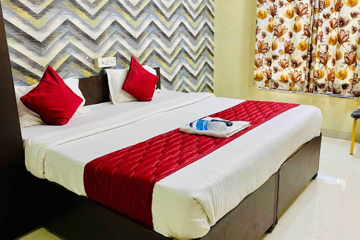 A neatly made bed with red and white bedding, a water bottle, and a towel on the bed.