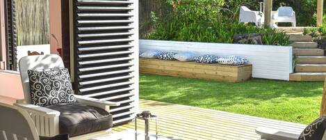 Área de pátio com móveis de exterior, deck de madeira, jardim, banco de madeira e plantas.