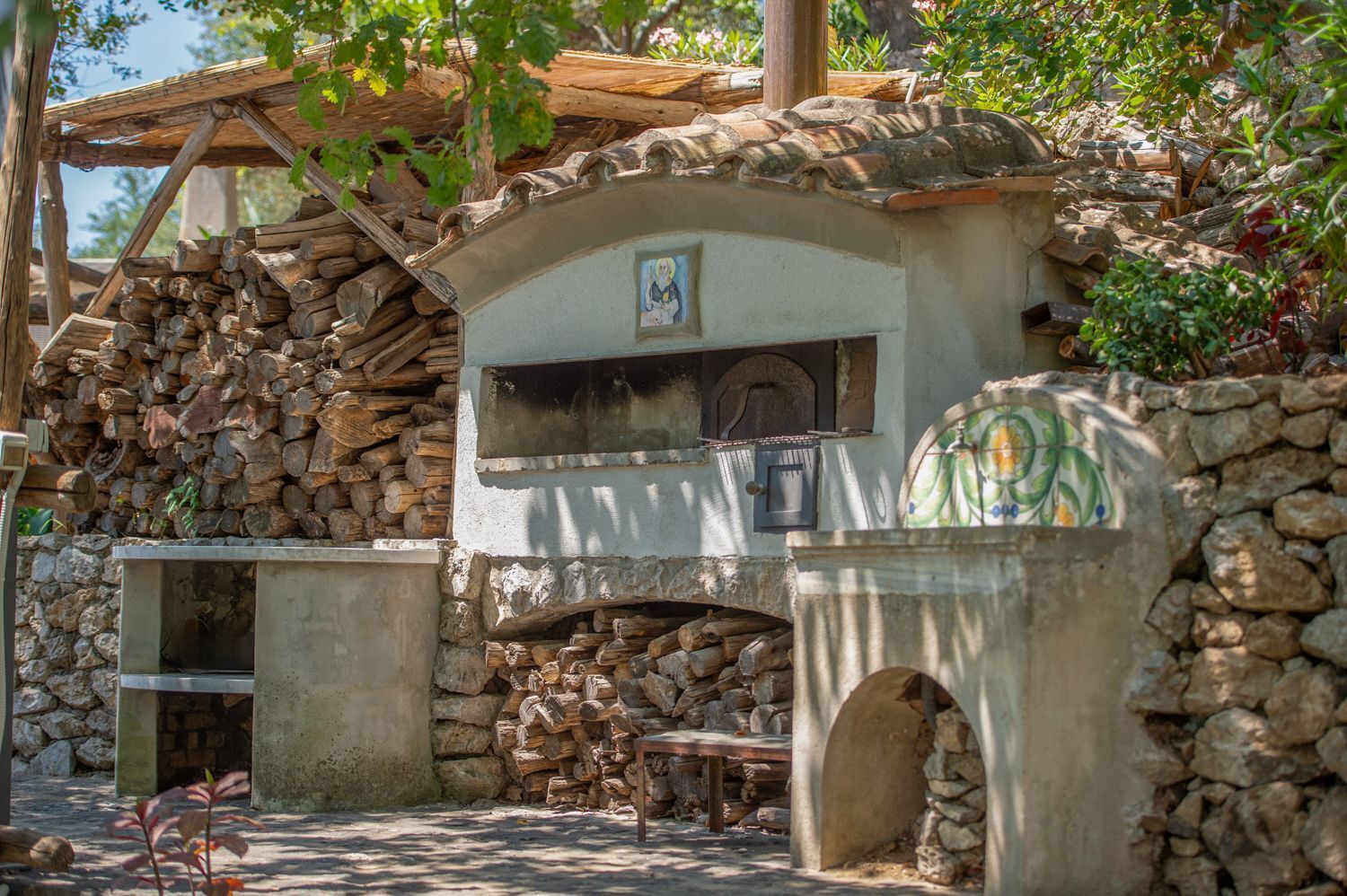 Une cuisine extérieure rustique, dotée d’un four en pierre, d’une pergola en bois et d’un mur en pierre.