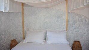 A bed with white linens and two pillows, a stone-textured wall, and a wooden headboard.