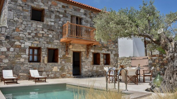 A stone building with a pool, outdoor seating, and a tree.