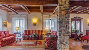 A spacious living room with a stone pillar, wooden beams, a red floral sofa, and a patterned rug.