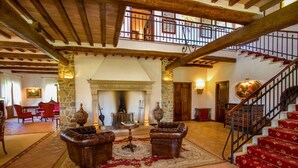 A spacious lobby with a fireplace, leather armchairs, a staircase, and a stone wall.