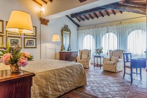 Une chambre spacieuse avec un grand lit, deux fauteuils, un bureau en bois et un miroir.