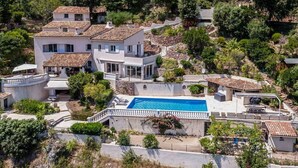 A large villa with a swimming pool, multiple terraces, and lush greenery surrounding the property.