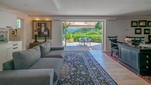 A modern living room with a sofa, a rug, a dining area with a table and chairs, and a kitchen area with a cabinet and a chair.