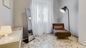 Quarto com cama, escrivaninha, luminária, espelho e janela com cortinas.