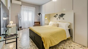 Quarto de hotel moderno com cama, escrivaninha, cadeira, luminária e um mapa-múndi na parede.