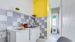 Uma cozinha compacta com pia, uma cafeteira vermelha e uma máquina de lavar no quarto vizinho.