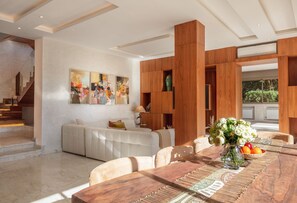 A modern living room with a dining area, wooden paneling, a staircase, and abstract art on the wall.