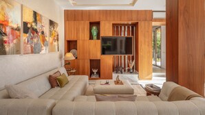 Een moderne woonkamer met een grote modulaire bank, een flatscreen televisie bevestigd aan een houten wand, en abstracte schilderijen.