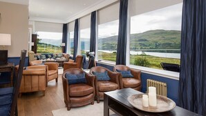 Un salón espacioso con sillones de cuero, una mesa de centro de madera y vistas a un lago y colinas.