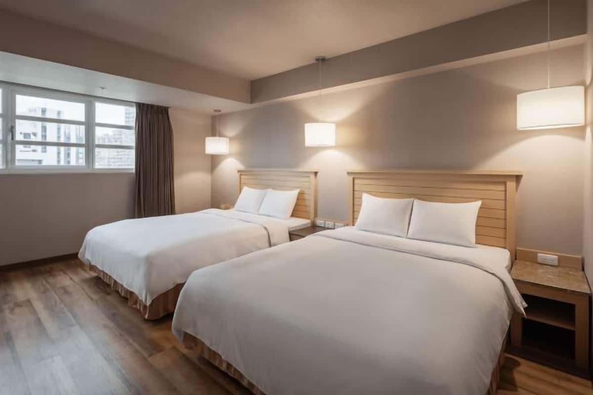 A hotel room with two beds, a window with curtains, and wall-mounted lights.