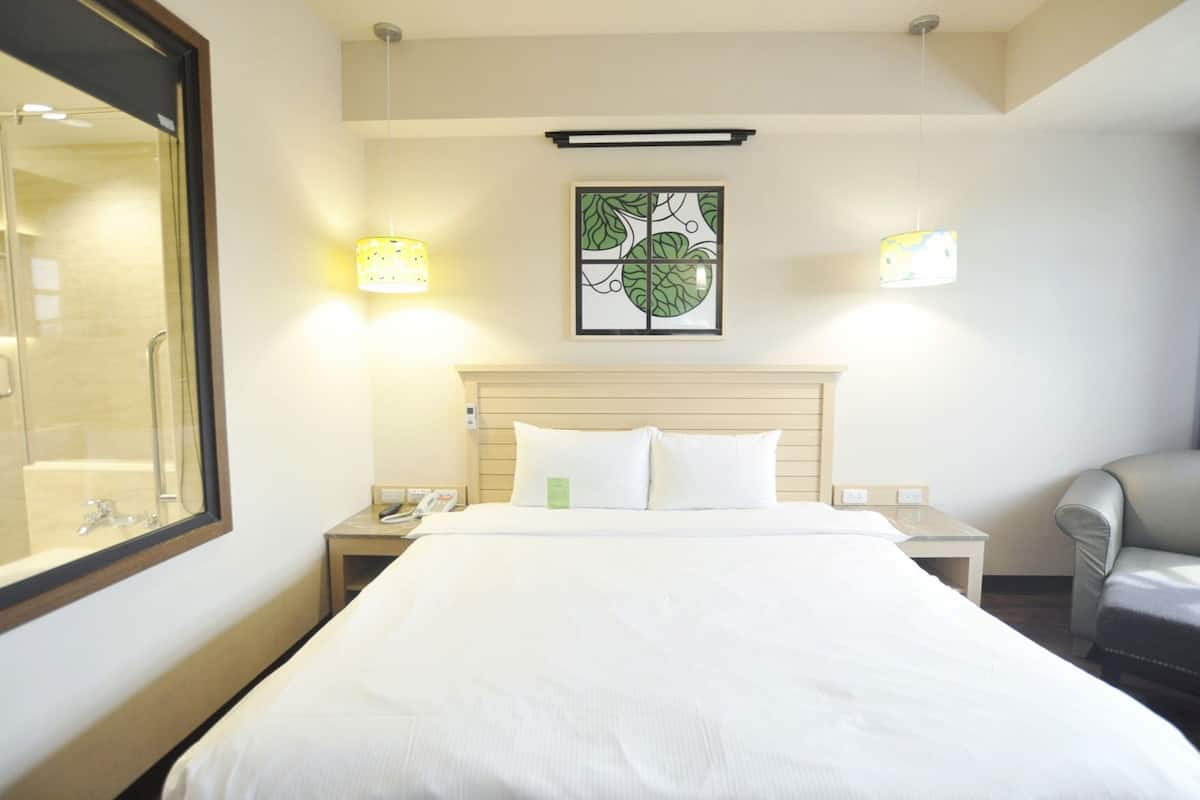 A hotel room with a large bed, bedside lamps, a nightstand with a phone, a chair, and a framed artwork on the wall.