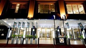 A hotel entrance with a large glass facade, a sign with Chinese characters, and potted plants at the entrance. - Kindness Hotel Qixian Kaohsiung (Kaohsiung)